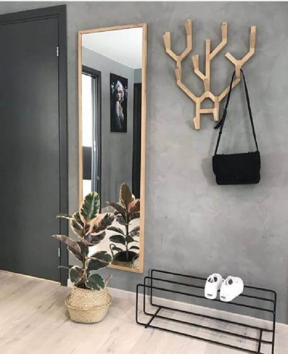 Hall com parede cinza, gancho de madeira para bolsa, sapateira preta, espelho e vaso de palha com planta