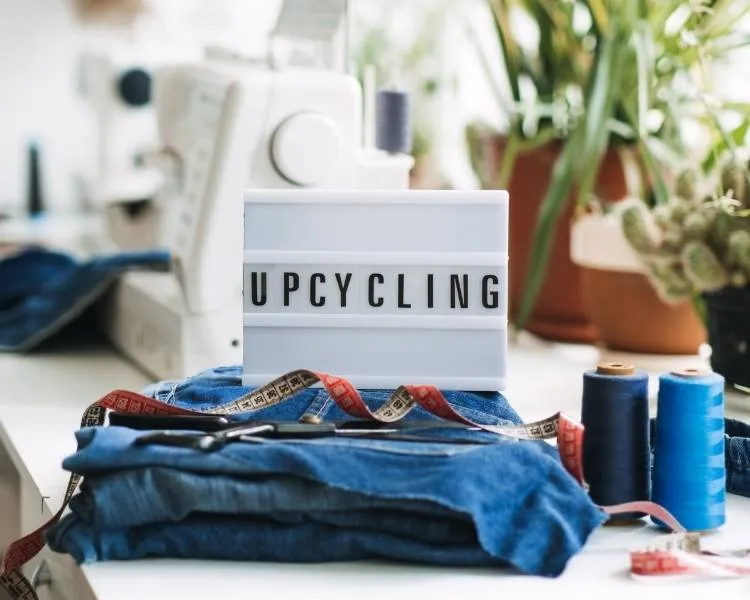 Upcycling: roupas velhas em mesa com fita métrica, linha, maquina de costura e plantas. Foto upcycling na moda.