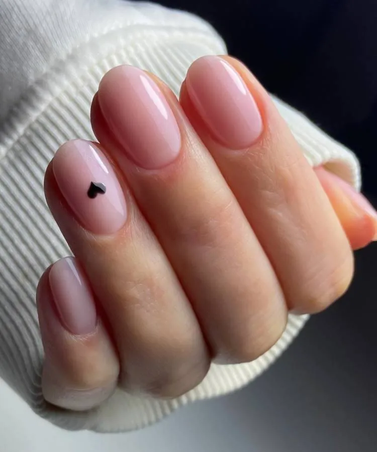 Mão feminina com unha rosa clara. Na filha única há um pequeno coração preto.
