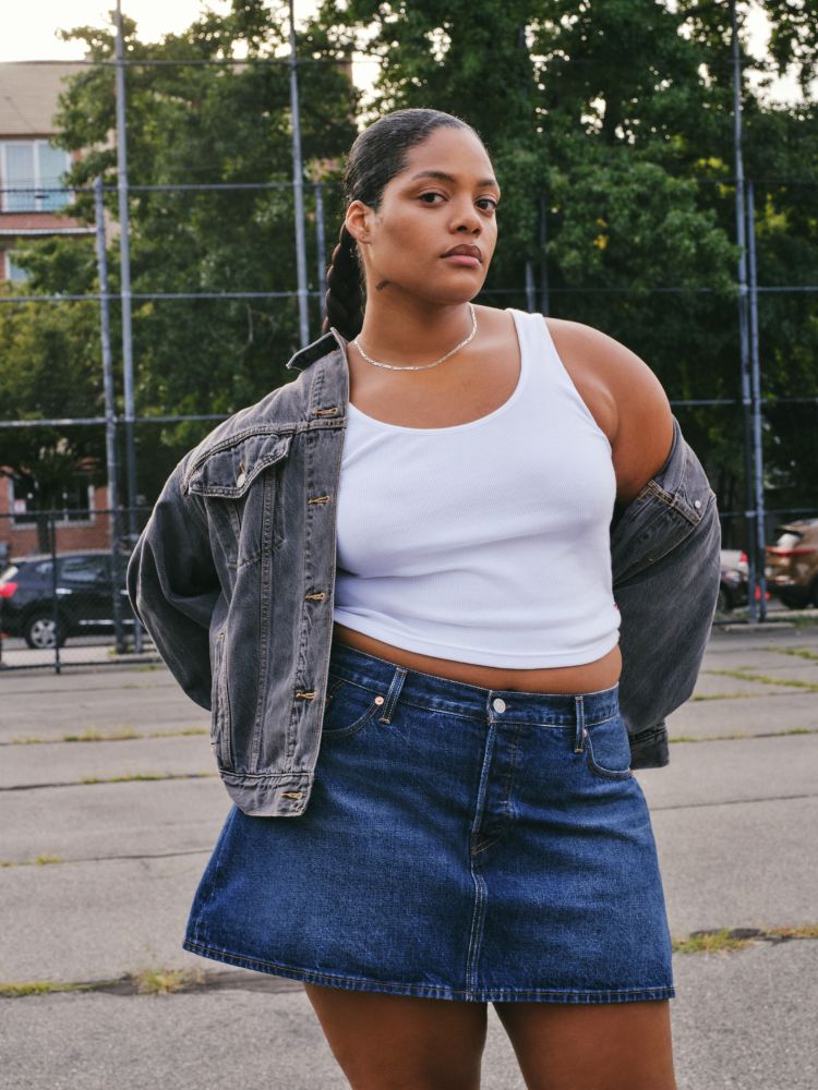 mulher usando regata branca, jaqueta jeans preta e saia jeans azul