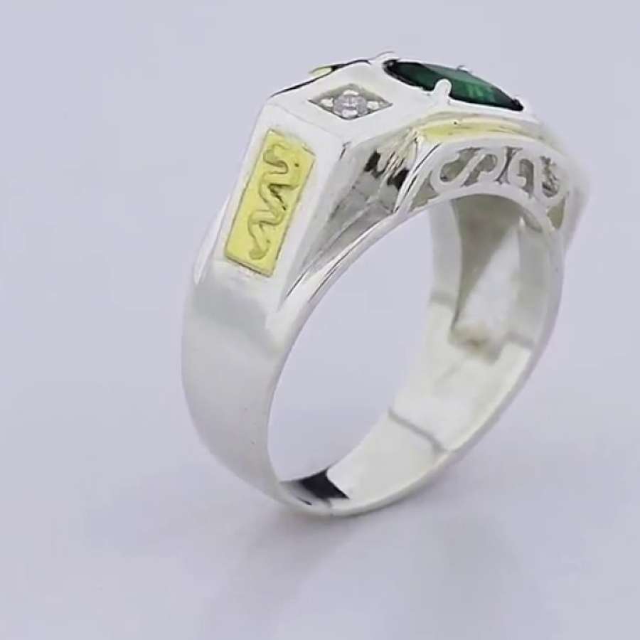 Anel masculino prateado com espaços vazados, pedra verde, símbolo da fisioterapia, detalhe em dourado e brilhante