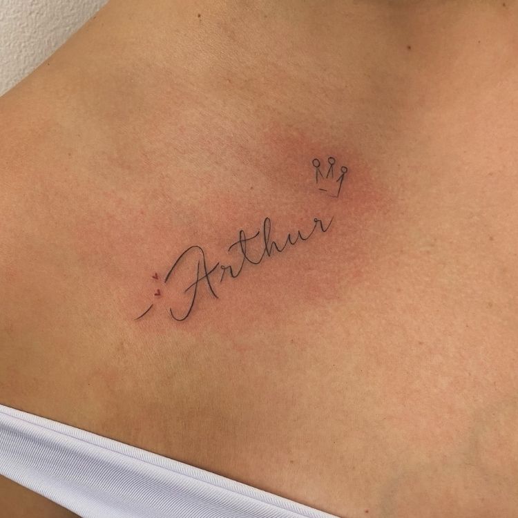 Foto de tatuagem escrito "Arthur" com uma coroa em ombro de pessoa de pele clara