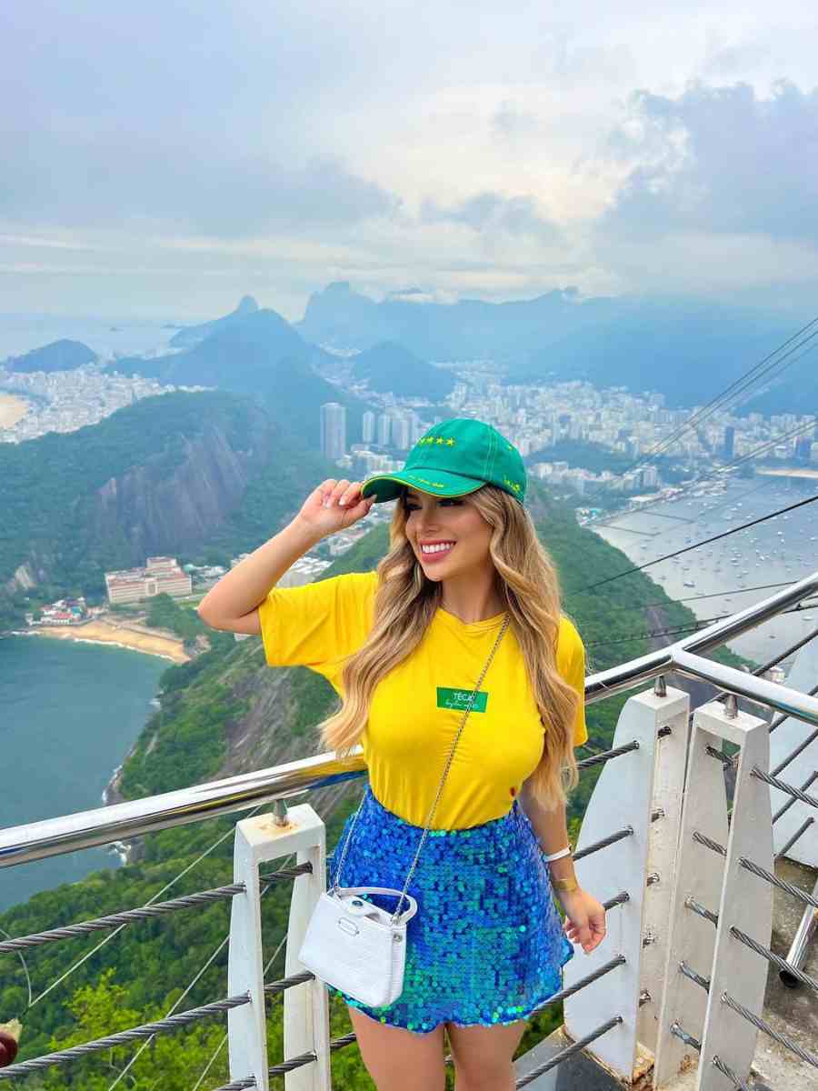 Foto de mulher usando camiseta amarela + boné verde + saia de paetes azul + bolsa branca.