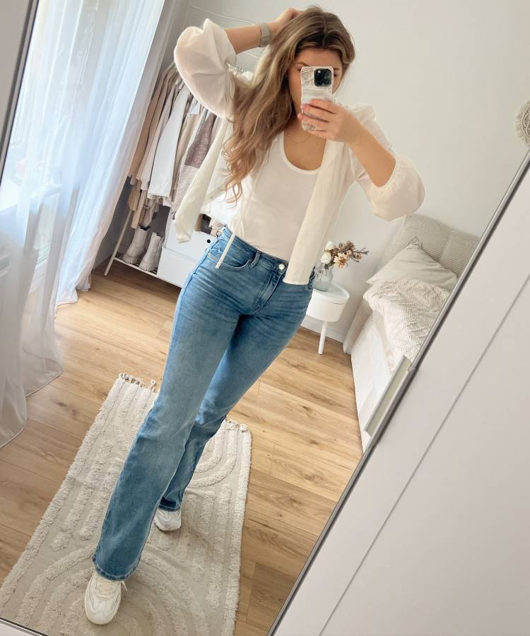 A imagem apresenta uma calça jeans skinny de corte reto, lavagem azul clara e cintura alta, tendência para 2025. O modelo clássico alonga a silhueta e combina perfeitamente com tênis branco e blusa básica, criando um visual casual e elegante.