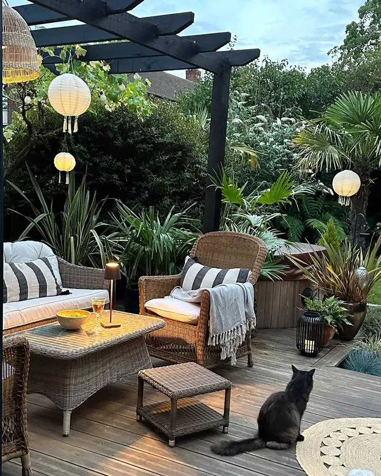 Área externa com poltronas de palha, almofadas, roupas reguladas e jardim decorado.