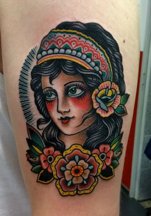 Tatuagem Old School de cigana com flor no cabelo preto e três flores coloridas abaixo