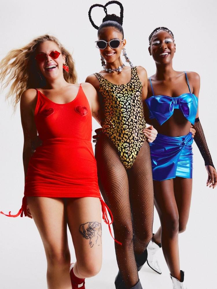 Três mulheres, sendo uma de pele clara e duas de pele negra, usando coleção de Carnaval da Riachuelo, como vestido vermelho, body animal print e conjunto azul de top de laço e saia 