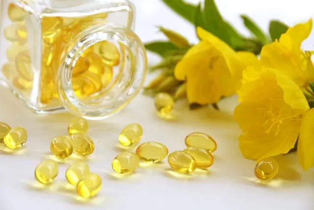 Frasco de vidro com capsulas de óleo de prímula ao lado da planta de origem do óleo