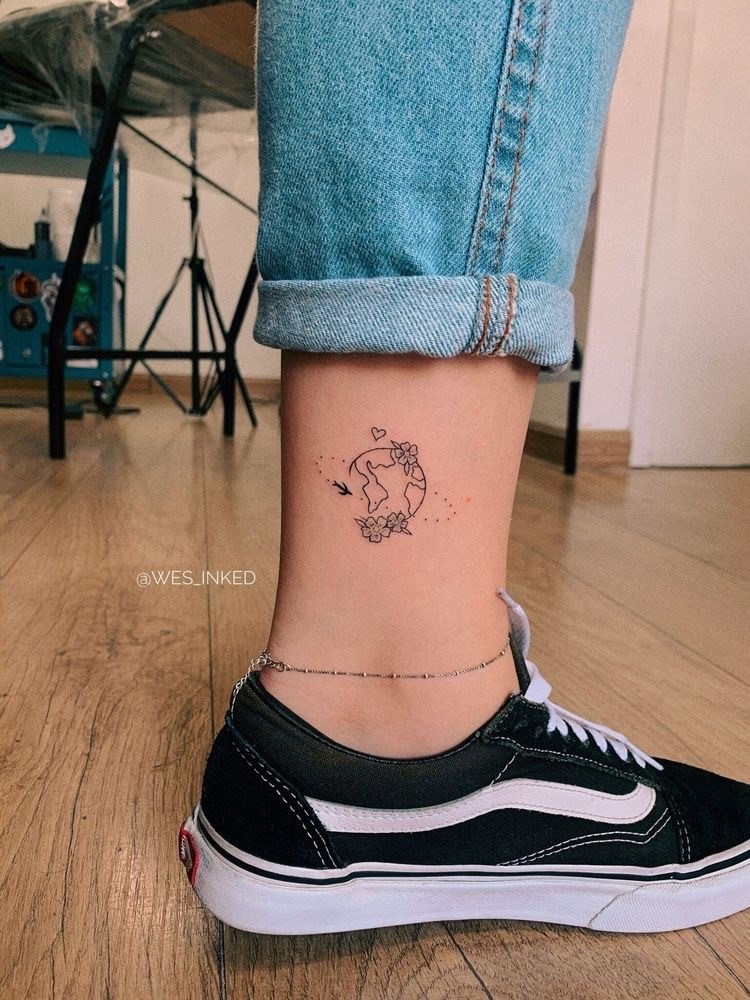 Mulher de pele clara com tatuagem de globo, flores, avião e coração na canela 