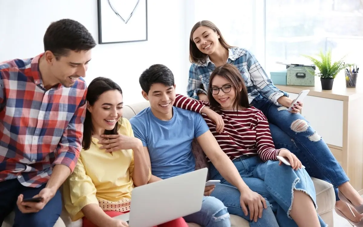 jovens interagindo em sofá de frente a um computador notebook