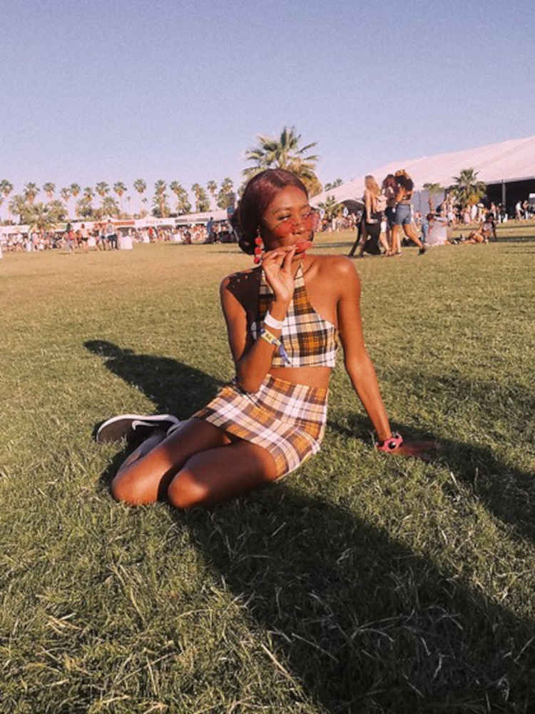 Mulher negra sentada em gramado usando conjunto de cropped e saia xadrez em marrom