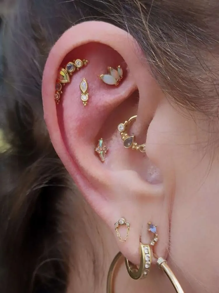 Orelha com piercing na hélix, scapha, rook, daith, conch e lóbulo, todos em dourado e em formatos de gotas