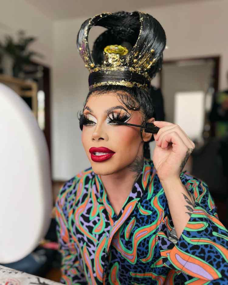 drag queen se maquiando, está passando máscara de cílios