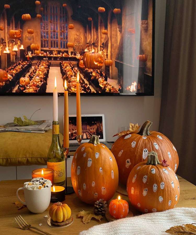 Mesa decorada com tema Halloween: abóboras pintadas à mão, velas, castiçal, bebidas, quadro