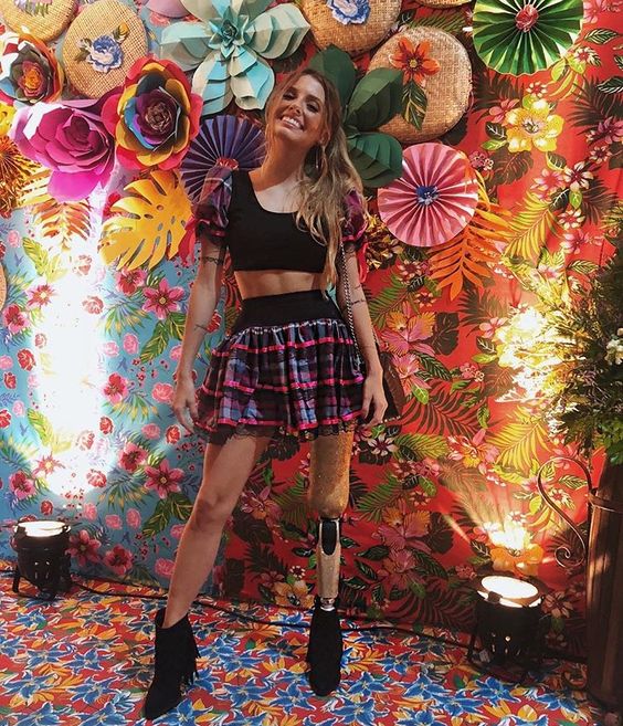 A imagem representa fundo para foto decorado com flores de papel, com mulher sorridente e look de festa junina na frente