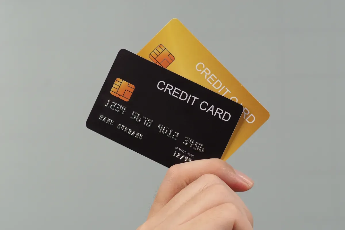 Pessoa segurando cartões de crédito preto e dourado associados a benefícios premium sem anuidade.