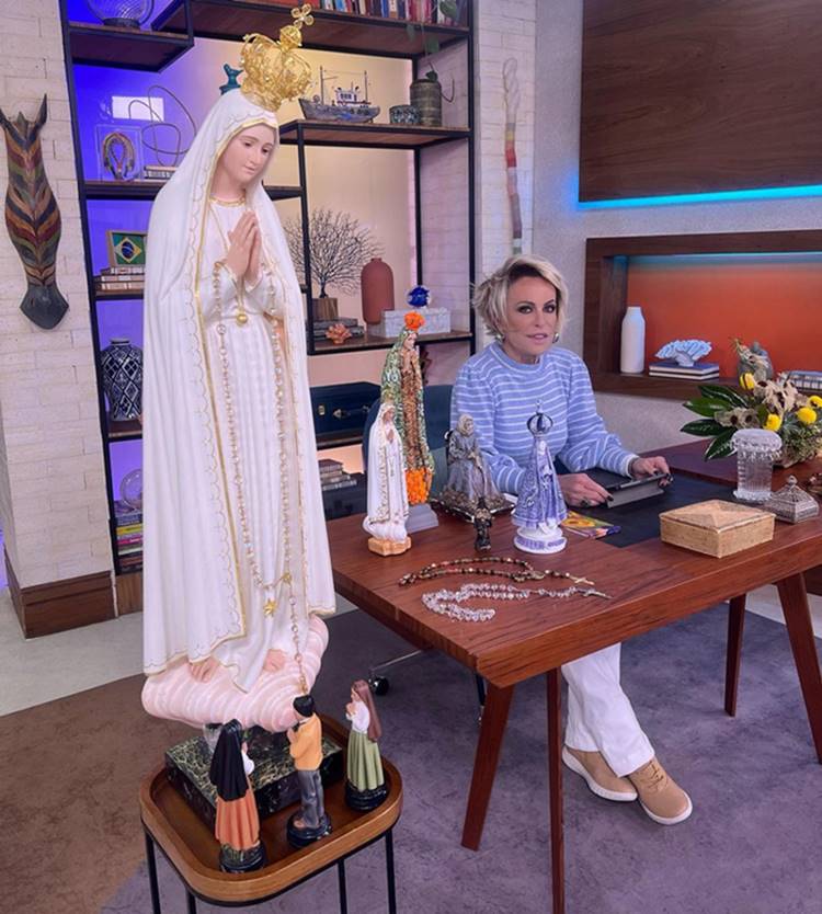 Apresentadora do Mais Vocês sentada em mesa no Mais Você, que contém várias imagens da senta Nossa Senhora do Rosário de Fátima