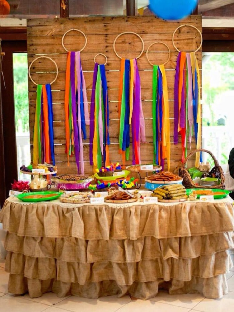 A imagem representa decoração de festa junina com bastidos, mesa cheia de doces típicos