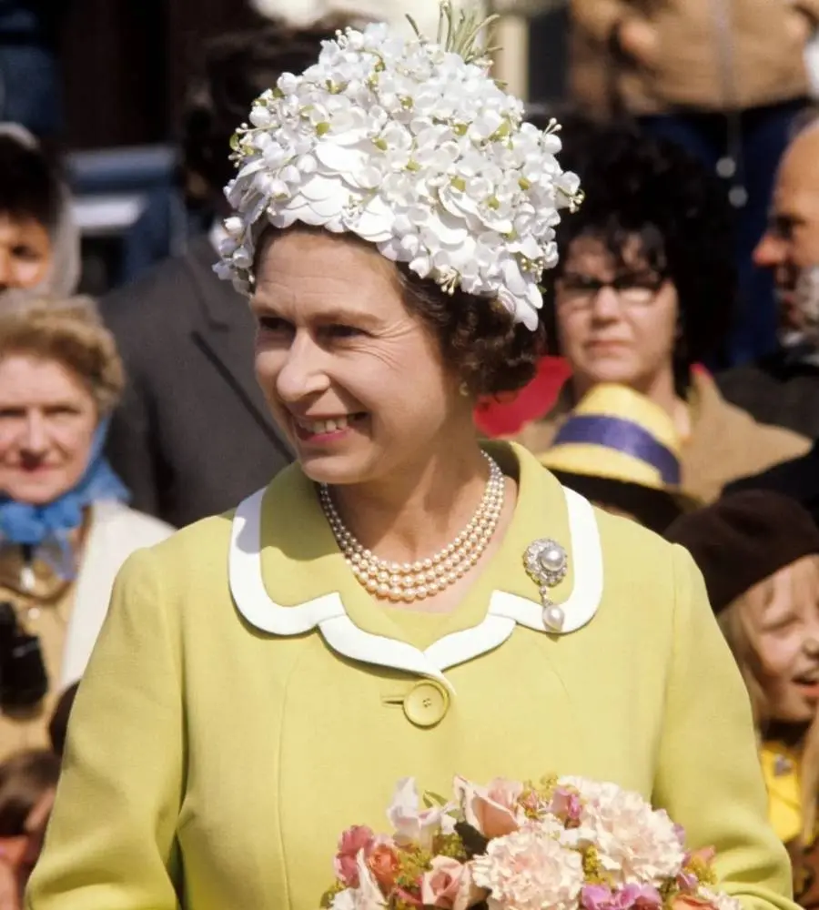 rainha Elizabeth em 1972 usando conjunto de alfaiataria amarelo e chapéu florido branco
