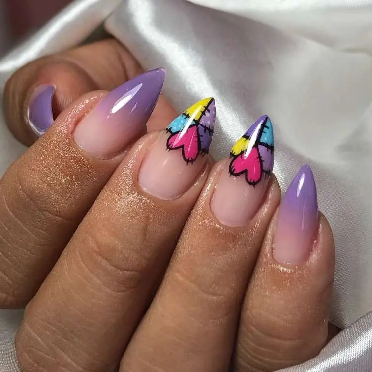 Unhas stiletto com design criativo. Duas unhas apresentam um degradê roxo e as outras duas têm pontas coloridas, com padrão de retalhos em amarelo, azul e rosa, delineado em preto.