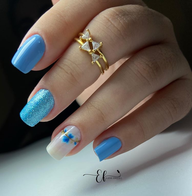 Unhas decoradas em tons de azul com Glitter e adesivo de flor