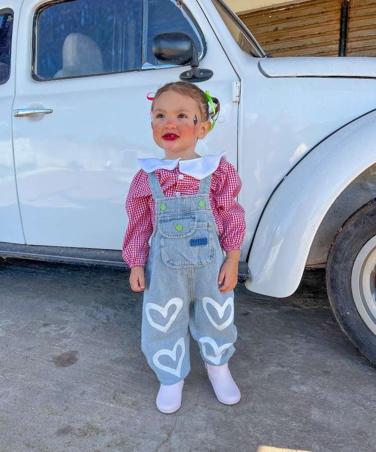 Menina com look de festa junina simples, usanco camisa xadrez com jardineira e make festa junina infantil