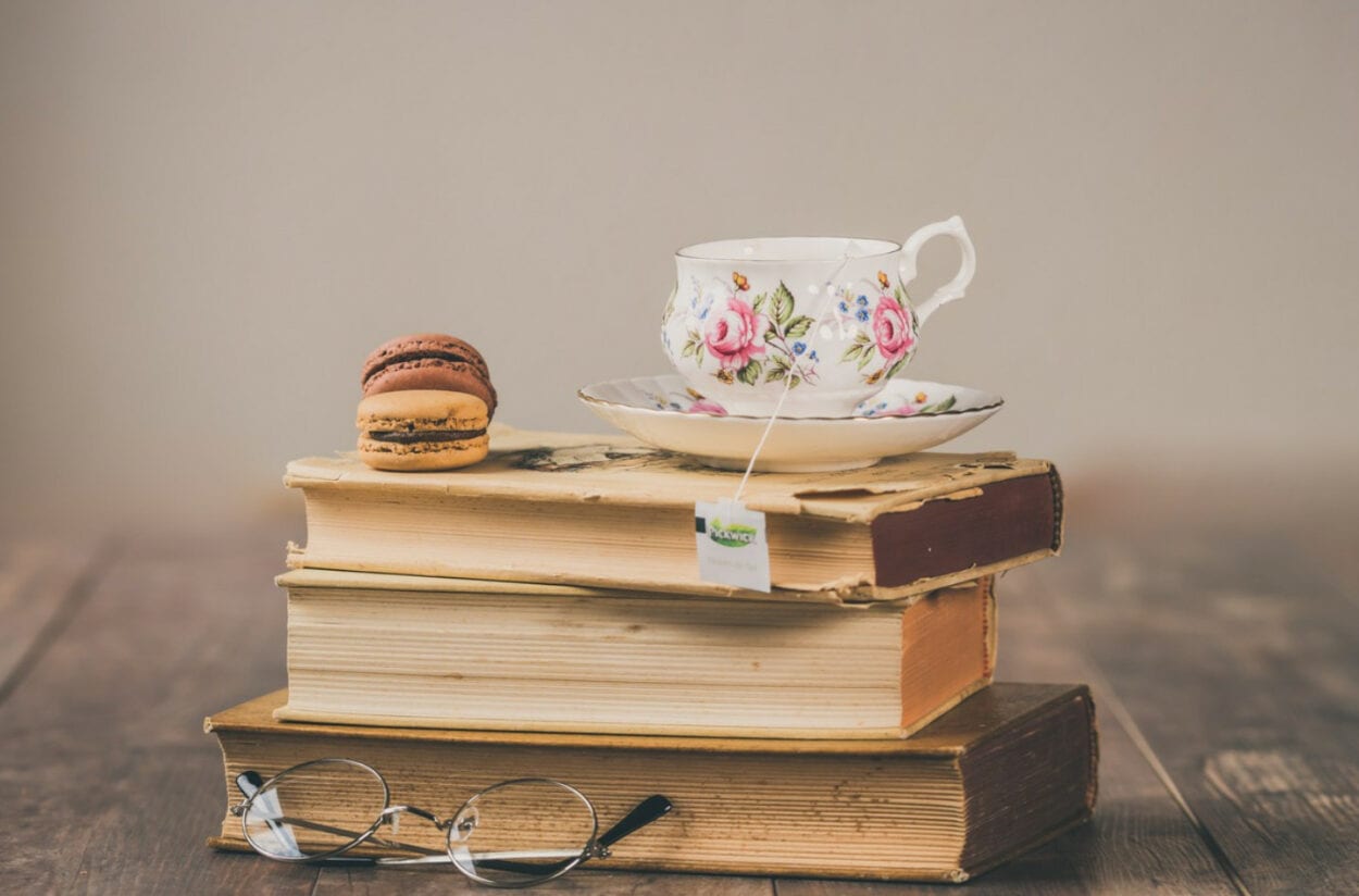 Pilha de 3 livros com dois macarrons, xícara de chá e óculos