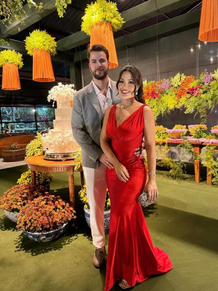 Gustavo usando terno cinza e Laís usando vestido vermelho, abraçados em buffet de casamento 