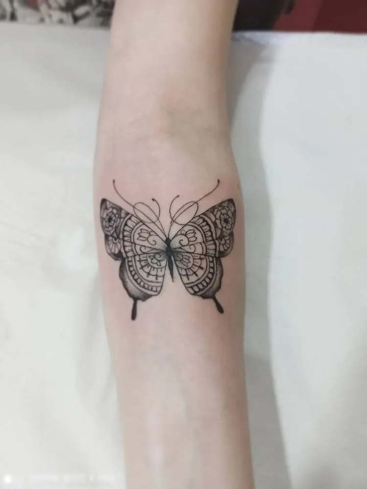 Tatuagem de traços finos cheia de detalhes nas asas. Feita no braço de uma mulher de pele branca. 