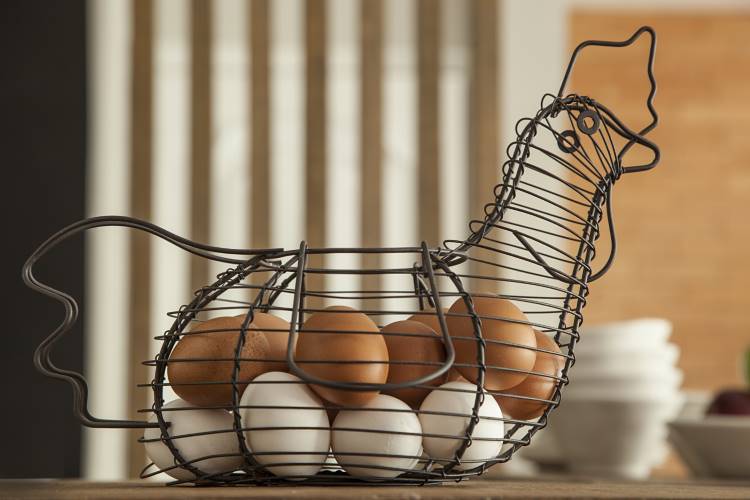 Nesta cozinha rústica moderna, uma cesta de ovos em forma de galinha, feita de metal preto, está cheia de ovos brancos e marrons. A cesta repousa sobre uma mesa de madeira.







