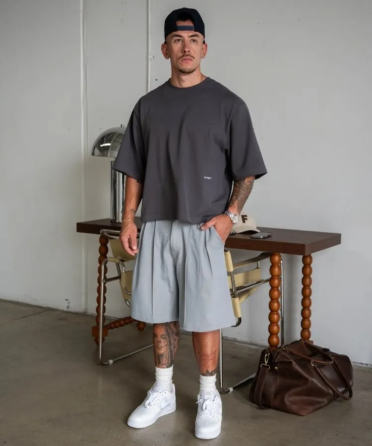 Influencer usando camiseta oversized cinza escura, bermuda relaxed cinza clara e tênis branco