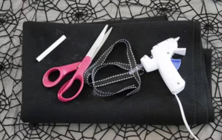Materiais para fazer a capa de Halloween: tesoura; fita; cola-quente. feltro preto 