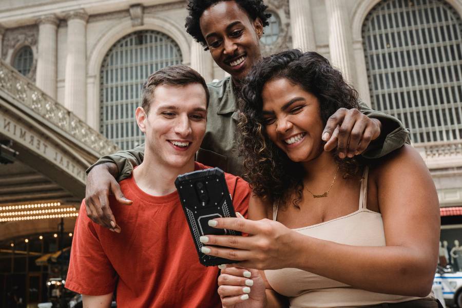 Três amigos sorrindo olhando para o celular.