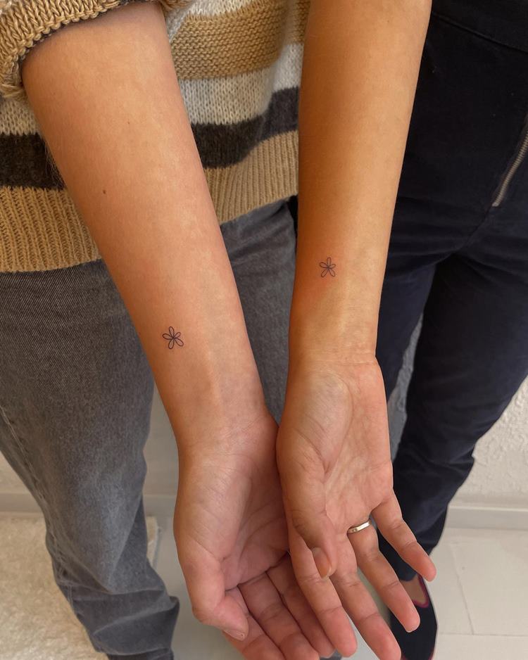 Tatuagem delicada de flor em braço, próximo do pulso, em dois braços