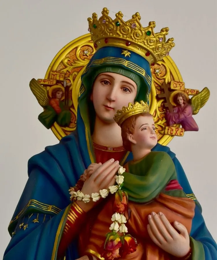 Imagem de Nossa Senhora do Perpétuo Socorro com manto azul, coroa dourada ornamentada e auréola intricada. Ela segura o Menino Jesus, que também usa coroa. Dois anjos ladeiam a imagem com símbolos sagrados sobre um fundo dourado detalhado.
