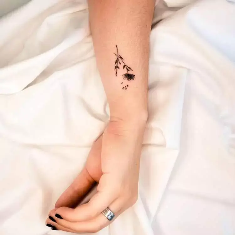 tatuagem de dente de leão na lateral de pulso de pessoa de pele clara 