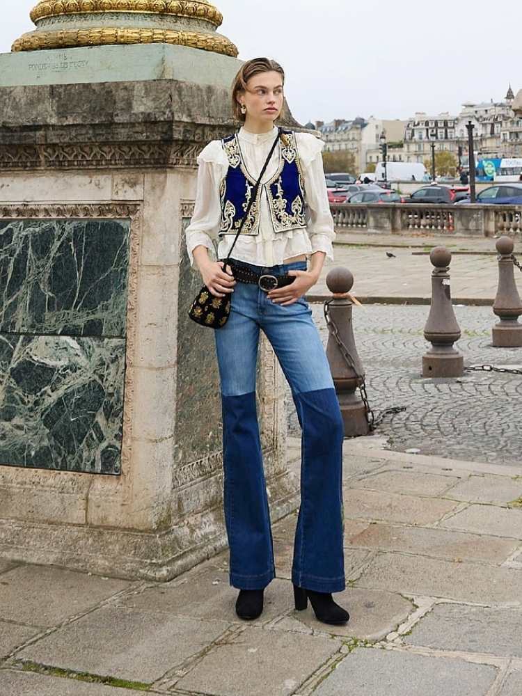 Mulher de pele clara usando camisa branca, colete de veludo azul e calça jeans azul 