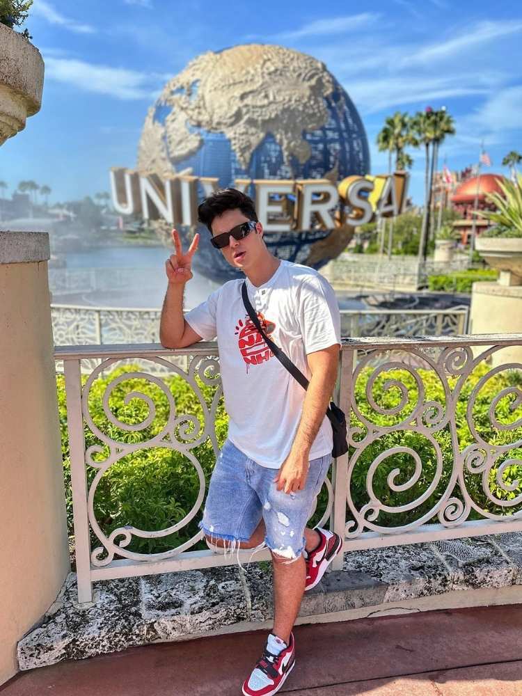Foto de Enaldinho usando blusa branca, bermuda jeans, em frente ao globo da Universal