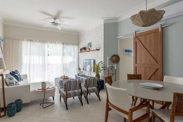 Sala de jantar e estar integrada com porta de correr de madeira, poltronas, sofá branco, mesa de jantar, tijolinho à vista, e itens de decoração. 