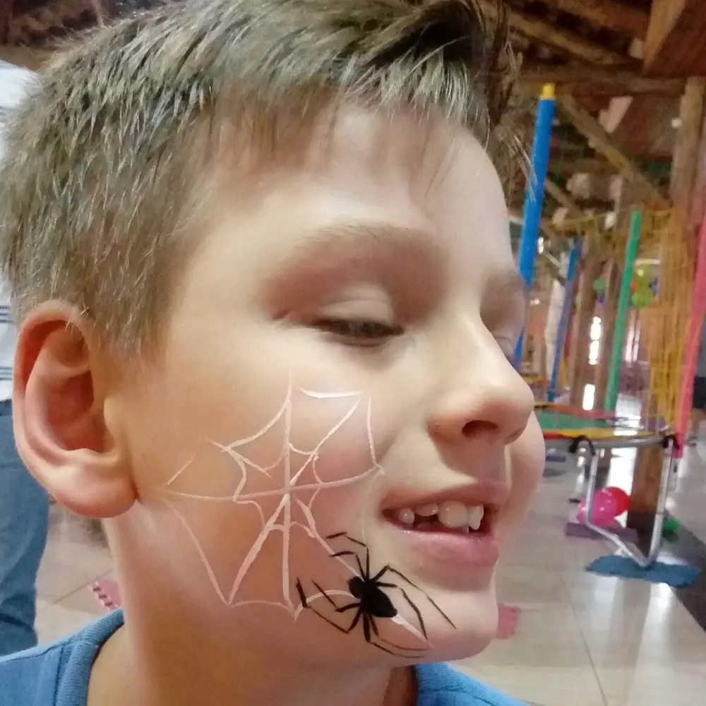 Menino com aranha desenhada no rosto em parque de diversões. Menino com aranha desenhada no rosto - Halloween em casa.