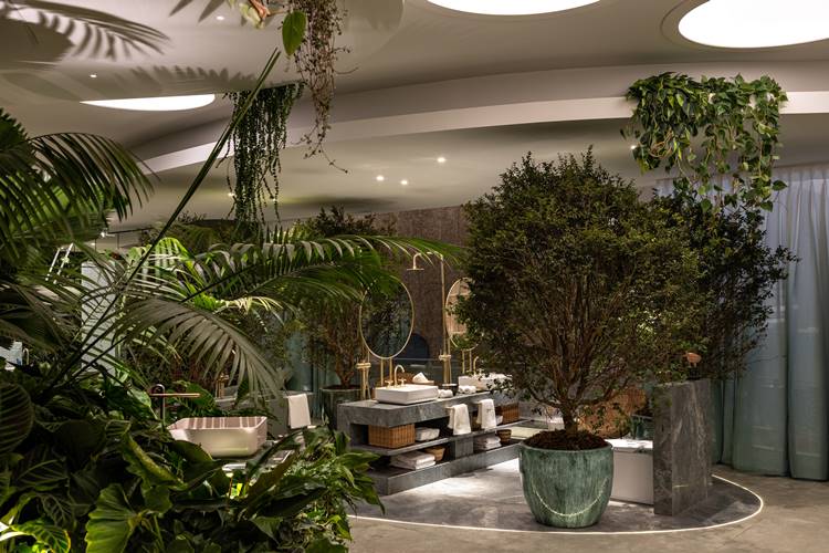 Banheiro com tons de cinza e dourado repleto de grandes plantas.