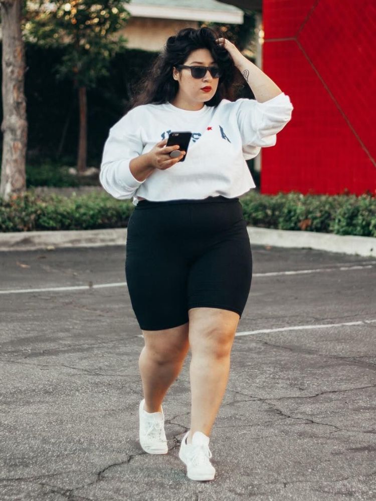 Mulher de pele clara com biker shorts preto, tênis e cropped branco