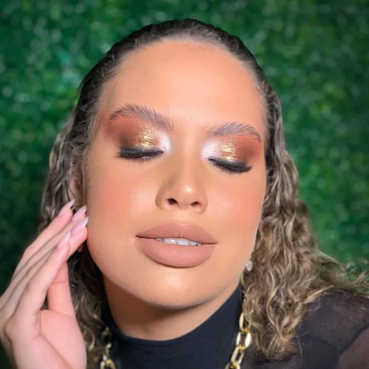 Mulher de pele clara com maquiagem dourada nos olhos e batom nude.