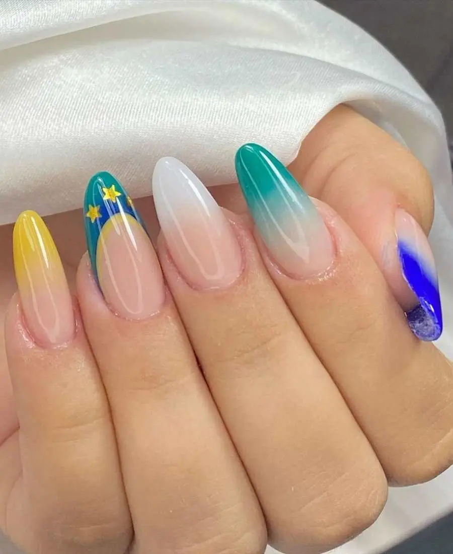 Imagem de mão com unhas decoradas para a Copa do Mundo 2022. Cores usadas, verde, amarelo, azul e branco. Polegar, francesinha azul-escuro. Indicador, francesinha verde. Médio, francesinha branca. Anelar, francesinha verde, azul e amarelo com estrelas. Mínimo, francesinha amarela.