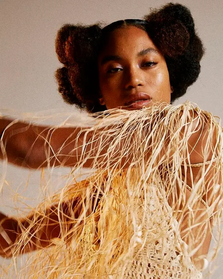 Modelo com uma blusa de tricot bege com detalhes em palha.