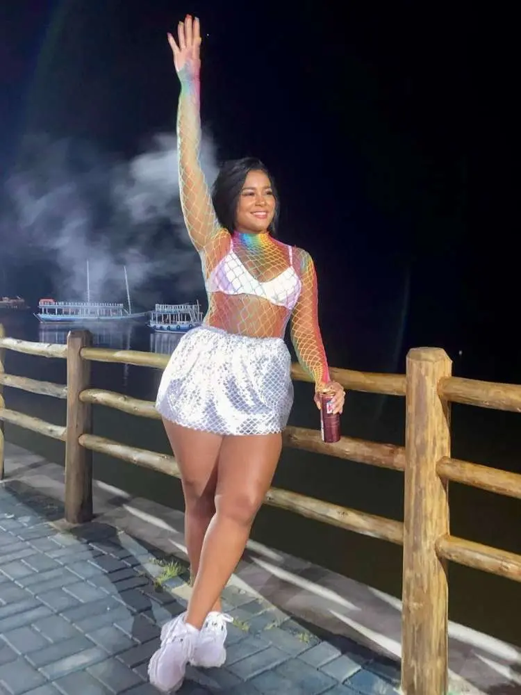 Mulher de pele morena usando body colorido transparente, top refletivo e saia prata