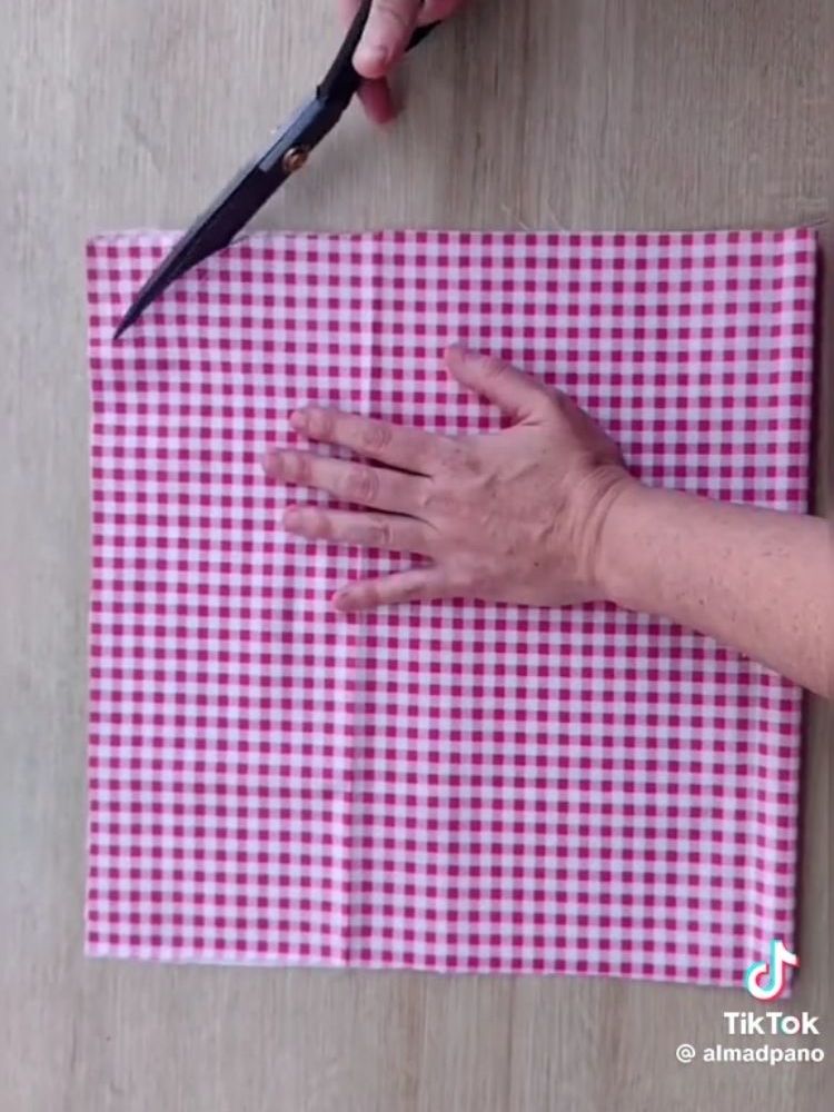 Pessoa de pele clara segurando tecido xadrez branco e rosa e cortando 