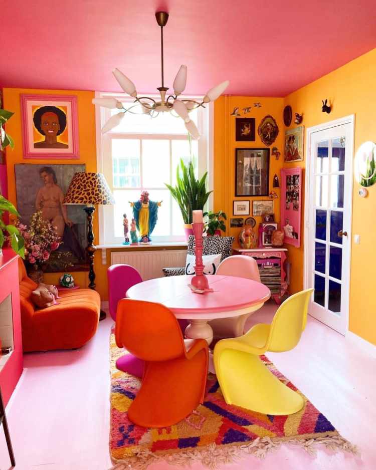 Sala com teto rosa, paredes laranjas, quadros coloridos, mesa rosa, poltrona de onça, cadeiras em tons de rosa, laranja e amarelo, poltrona laranja, tapete colorido e mais