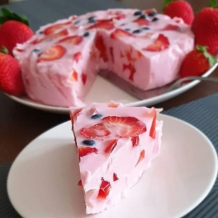 Fatia de doce vermelho encorpado com morango e mirtilo e o resto do bolo em um refratário ao fundo