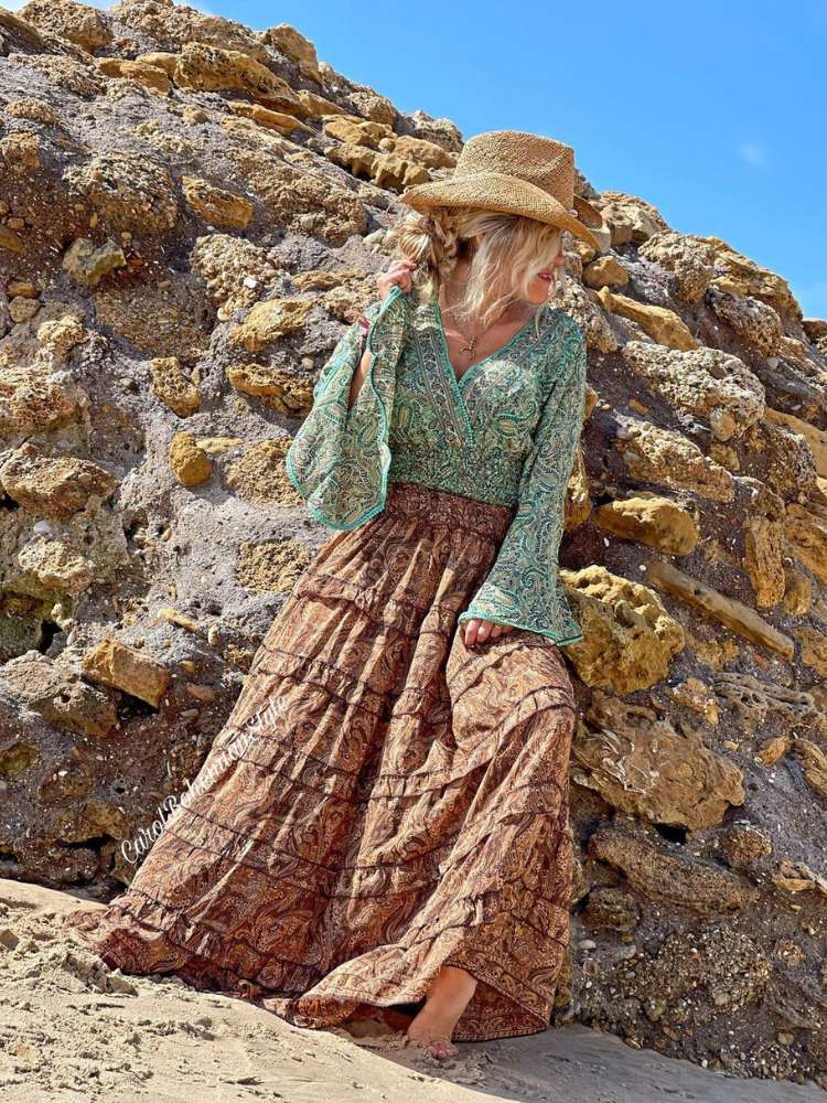 Mulher em pedras usando blusa boca de sino verde e saia marrom com camadas